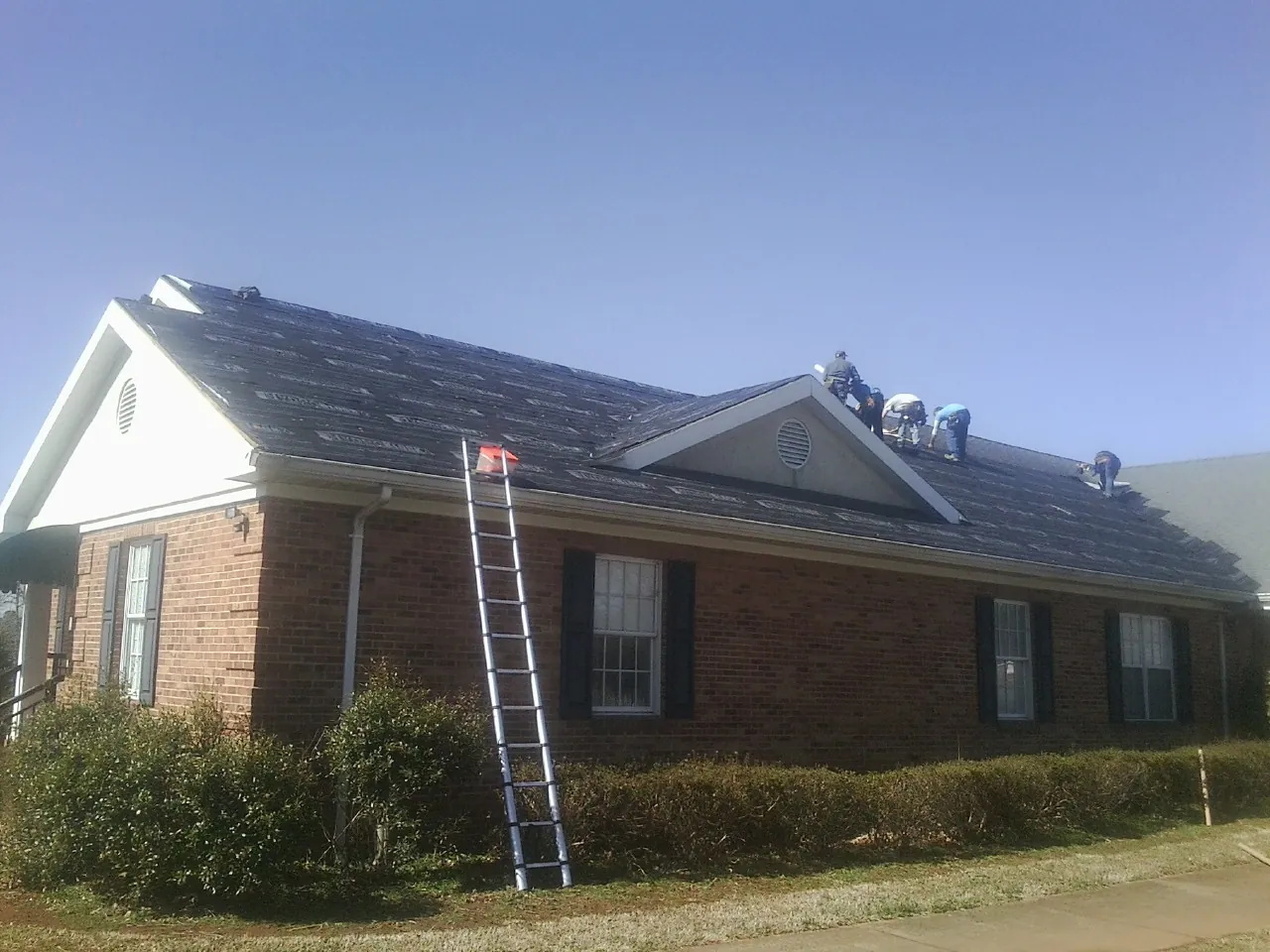 Crew tearing shingles off a brick ranch roof with a ladder set — Emergency Roof Repair work by our crew in Kooskia