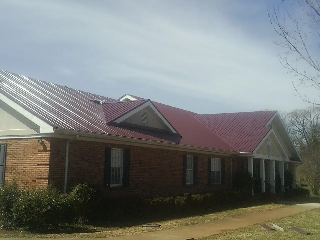 Red metal roof with gabled entries on a long brick building, from a Hail Damage Roof Repair job in Kooskia