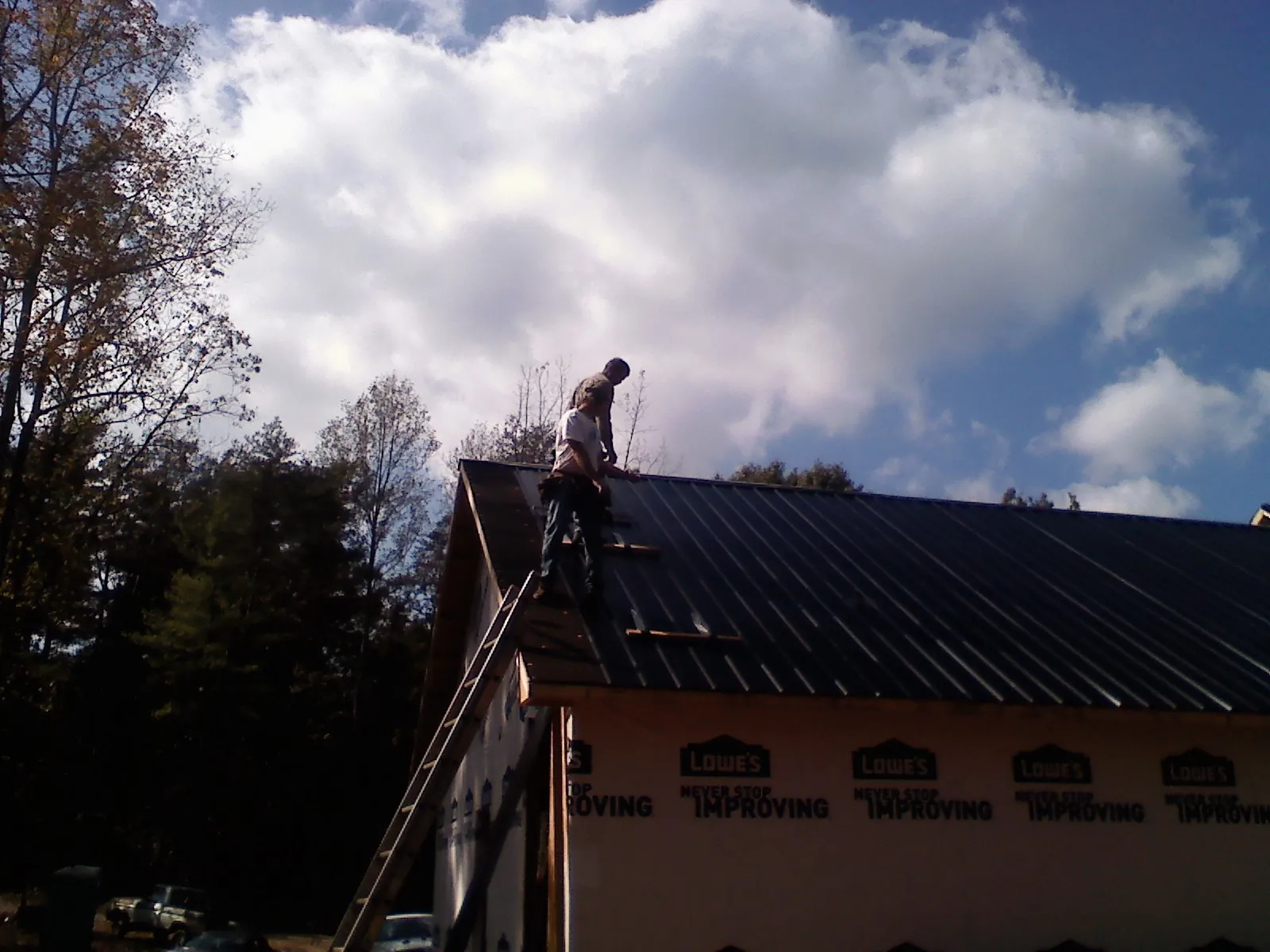 Roofer fastening dark metal panels high against a cloudy sky, from a Roof Inspection job in Kooskia