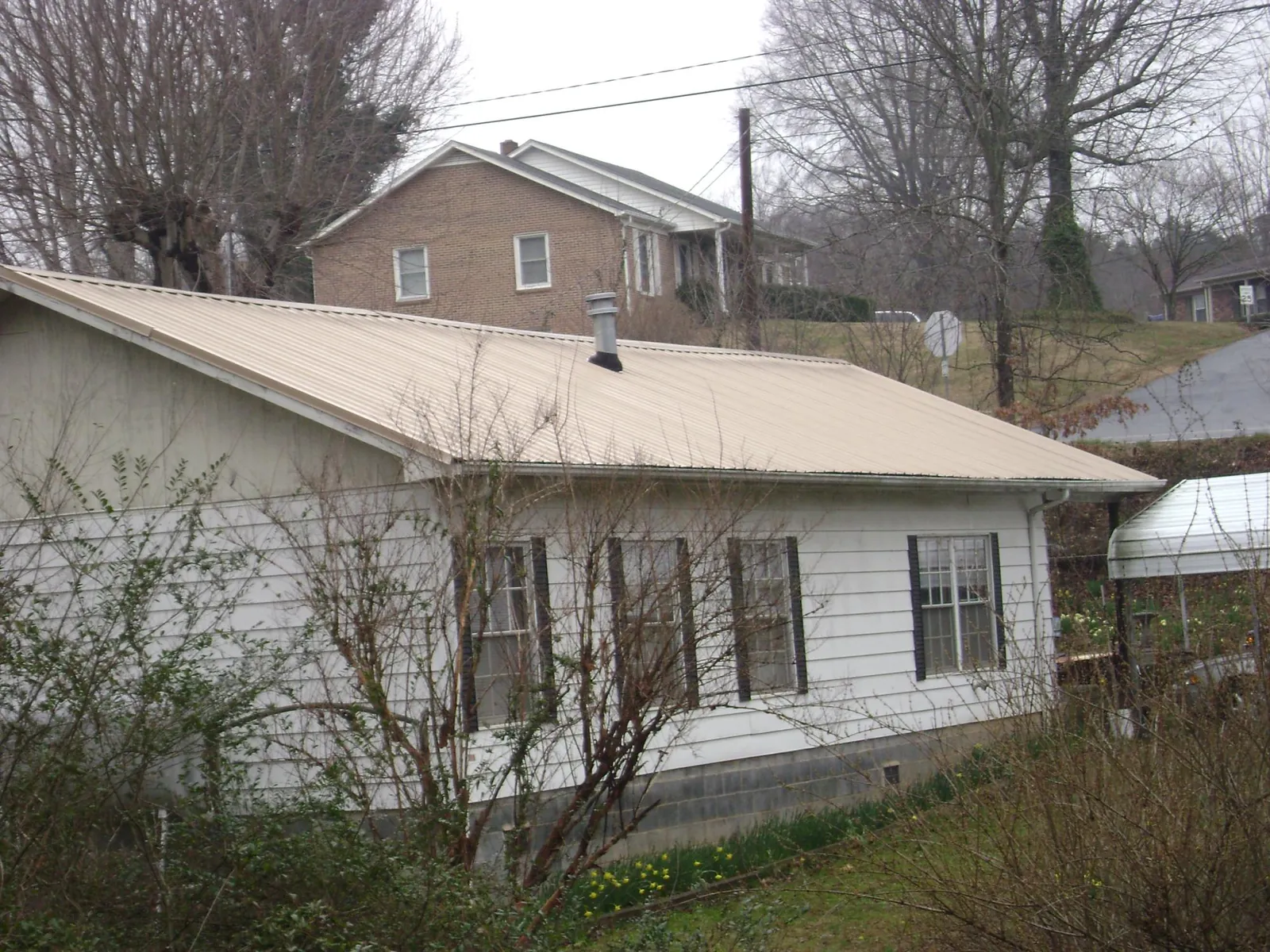 Tan metal roof on a white sided house set into a hillside — Commercial Roofing by Roofing Brothers in Kooskia
